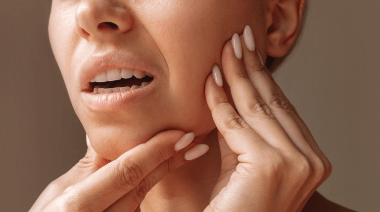 Woman experiencing jaw pain, touching her cheek, possibly due to jaw clenching.